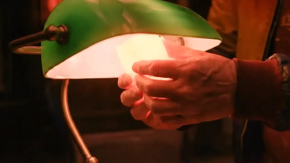 A hand slipping a red Moodie over the bulb in a green banker’s lamp, from the Legal Review commercial